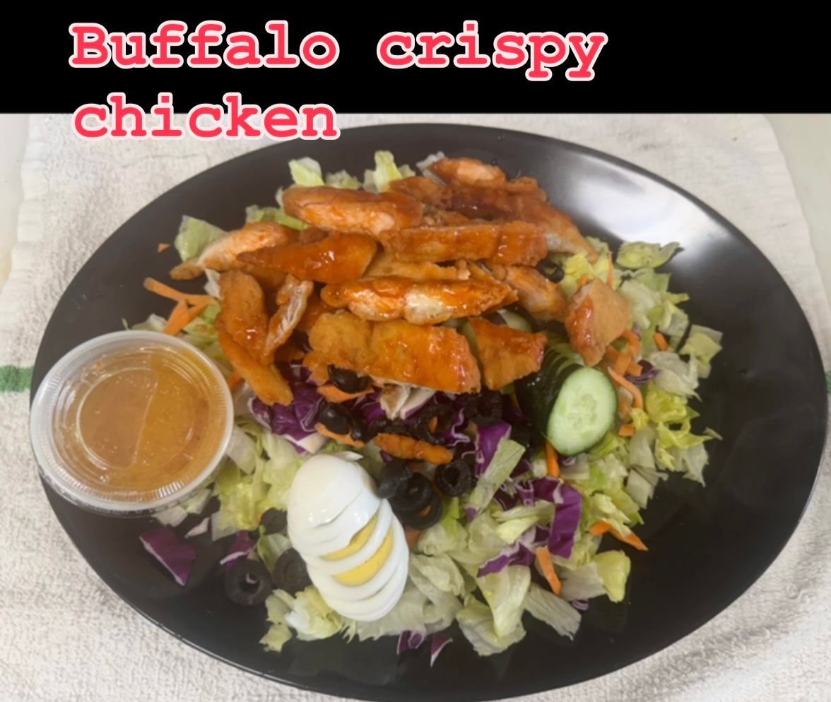 Salad with fried chicken, egg, vegetables, dressing in a container, on a black plate.