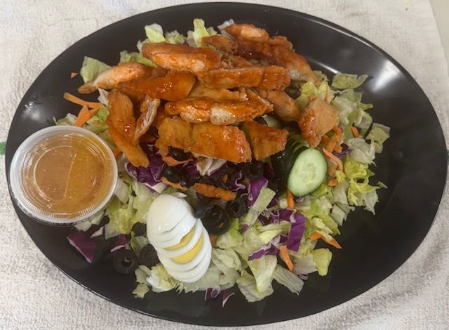 Salad with fried chicken, egg, and dressing on a black plate.