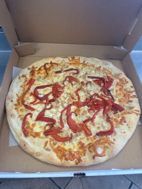 Pizza with red peppers and cheese in a cardboard box.