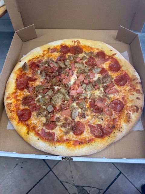 Pizza in a cardboard box, topped with pepperoni and other meats.
