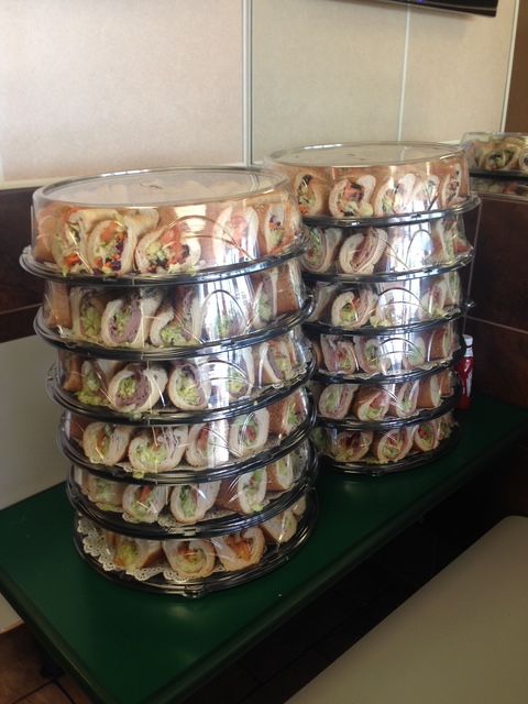 Stacks of wrapped sandwich platters on a green surface, ready for catering.