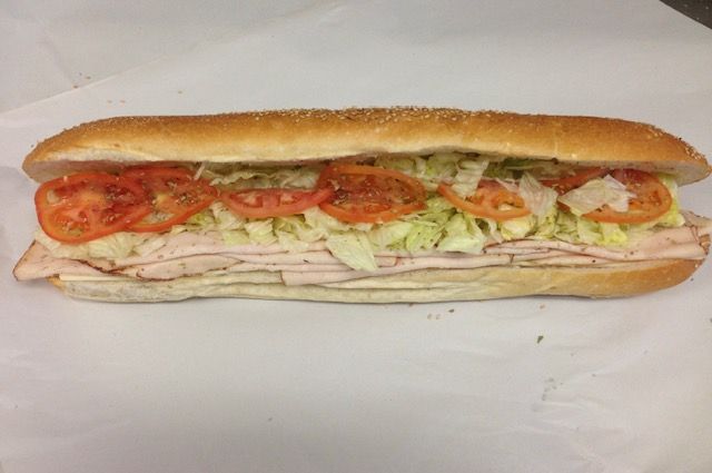 Sub sandwich on white paper with sliced tomatoes, lettuce, and meat.
