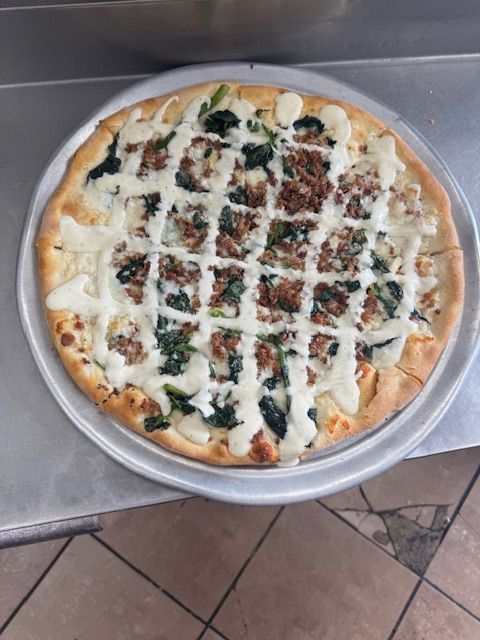 White pizza with sausage, spinach, and a white sauce grid pattern on a metal pan.