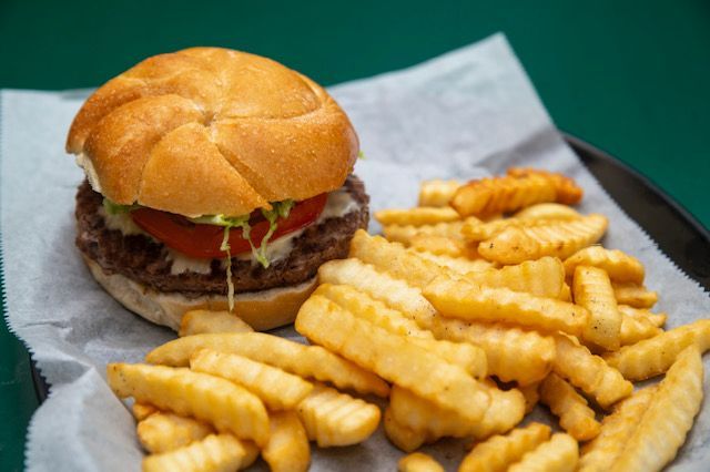 Burger with tomato and lettuce on a bun, served with crinkle-cut fries on a tray.
