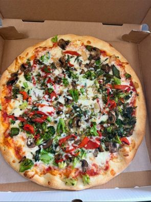 Vegetable pizza in a cardboard box; topped with broccoli, red peppers, and mushrooms.