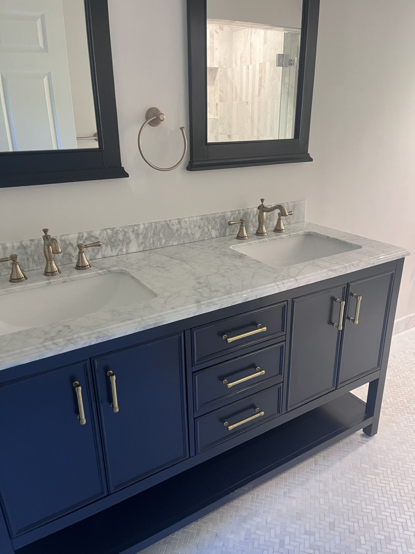 A double bathroom vanity with a white marble countertop, navy blue cabinets, gold hardware, and two black-framed mirrors.
