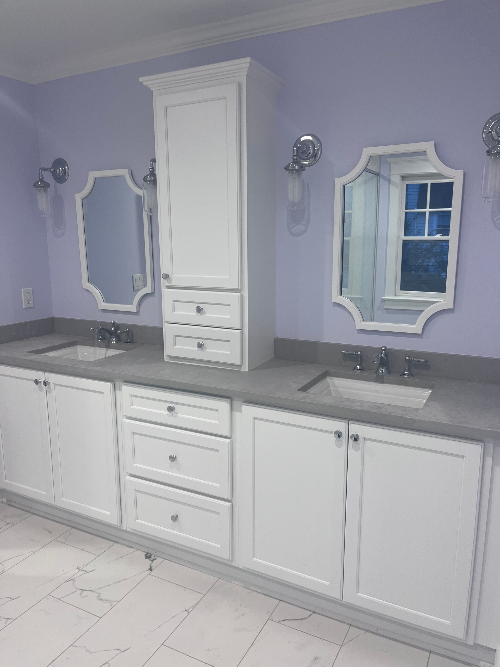 A double-sink bathroom vanity with white cabinets, gray countertops, and two white mirrors against lavender walls.