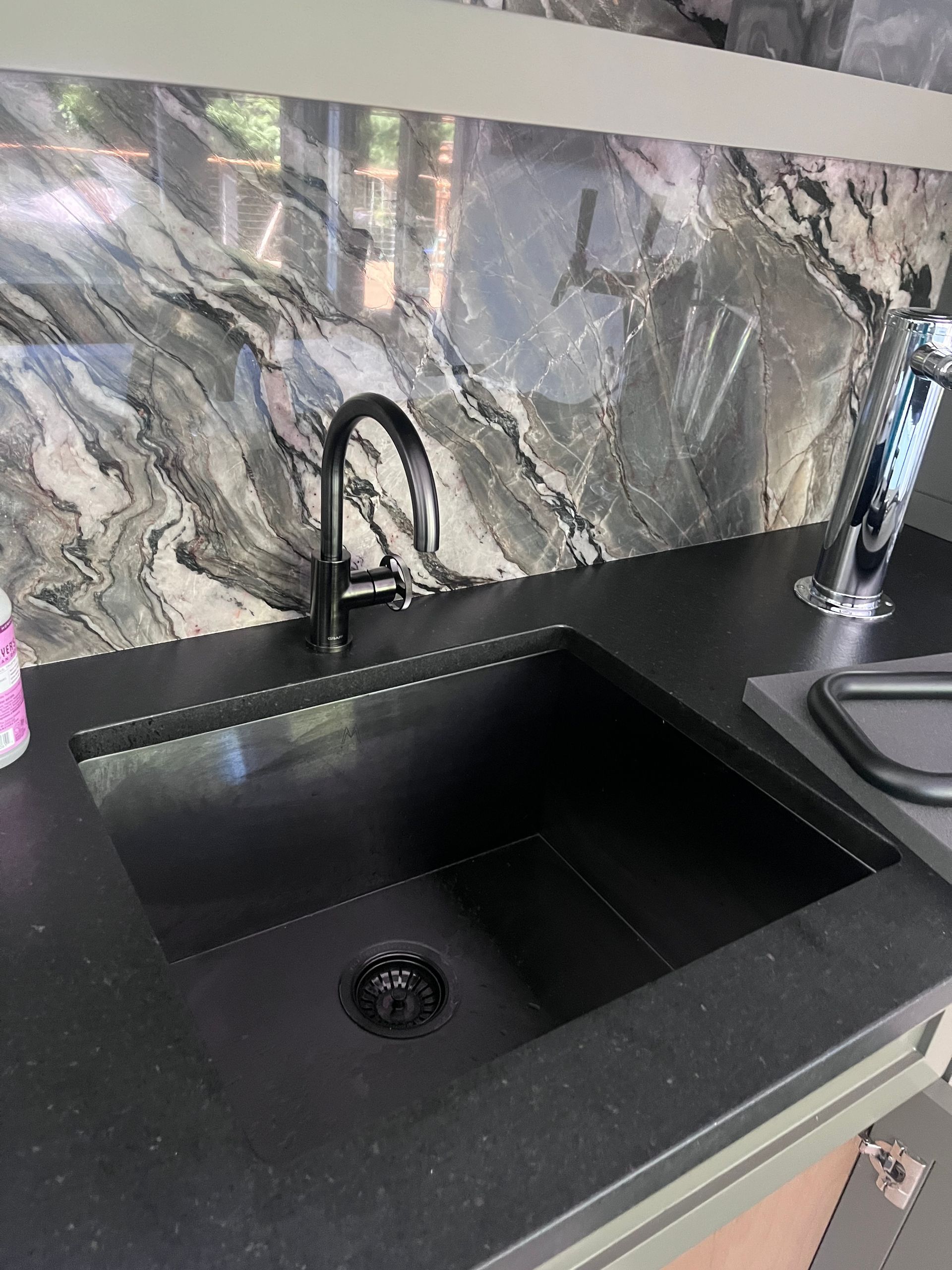 A matte black kitchen sink and matching faucet set against a dark, marbled stone backsplash and countertop.