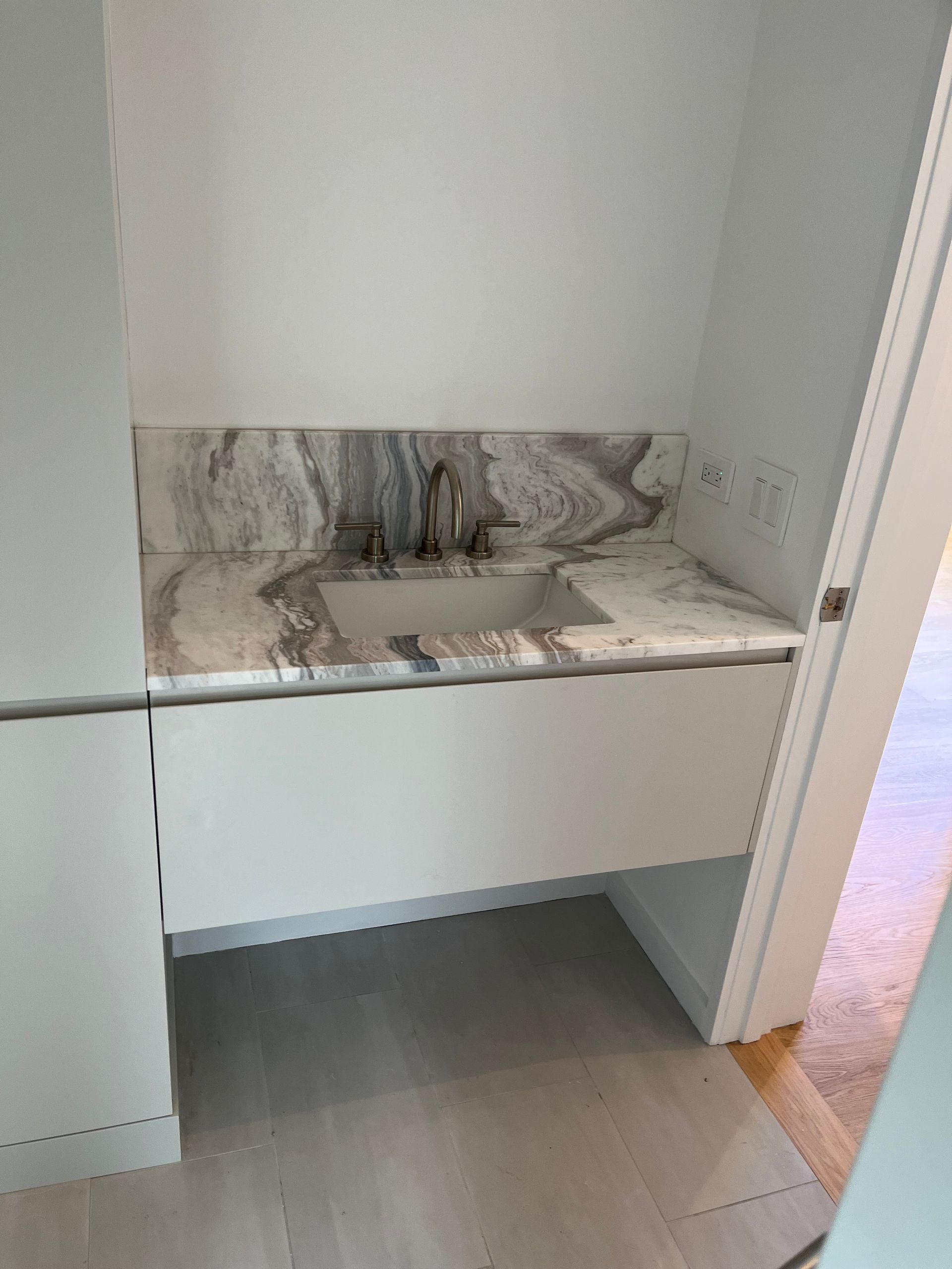 A modern floating bathroom vanity with a white cabinet, integrated sink, and a decorative marble backsplash.