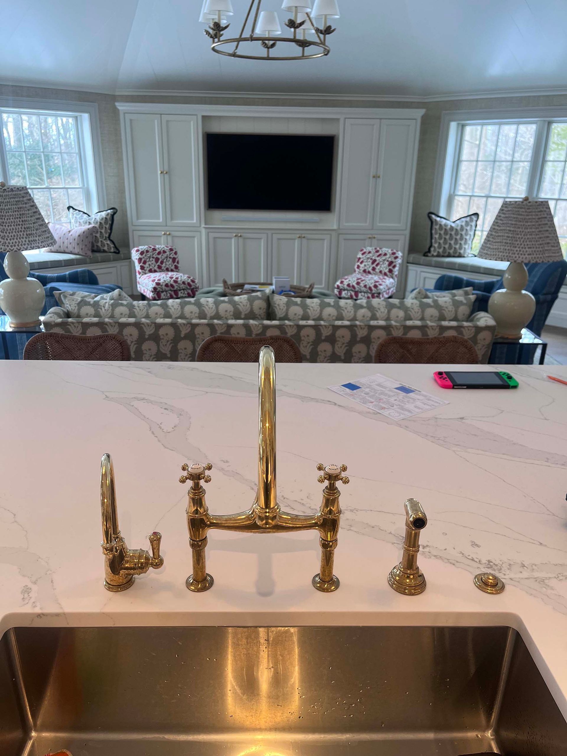Kitchen island with gold faucet, stainless steel sink, and a view of a living area with TV and sofa.