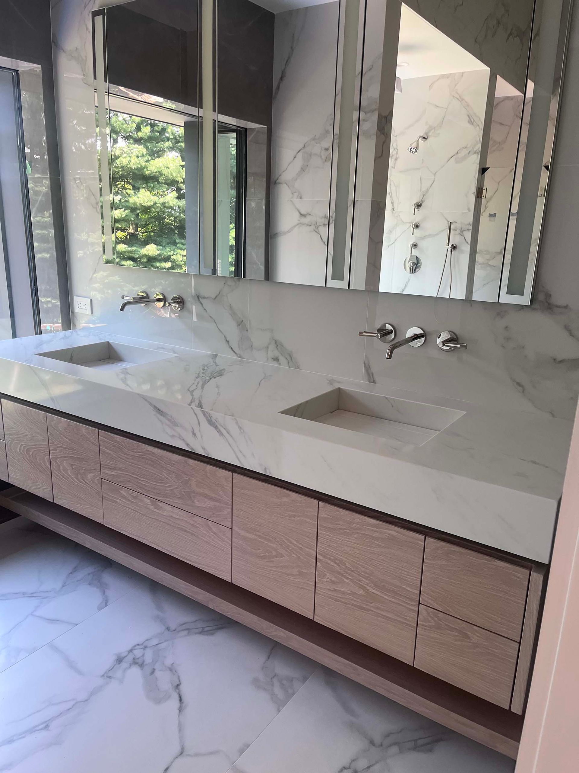 Modern bathroom with double vanity, marble countertops, wooden cabinets, and large mirrors.
