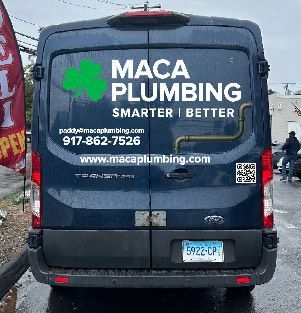 Rear view of a dark blue Maca Plumbing van, with logo and contact information on the back doors.