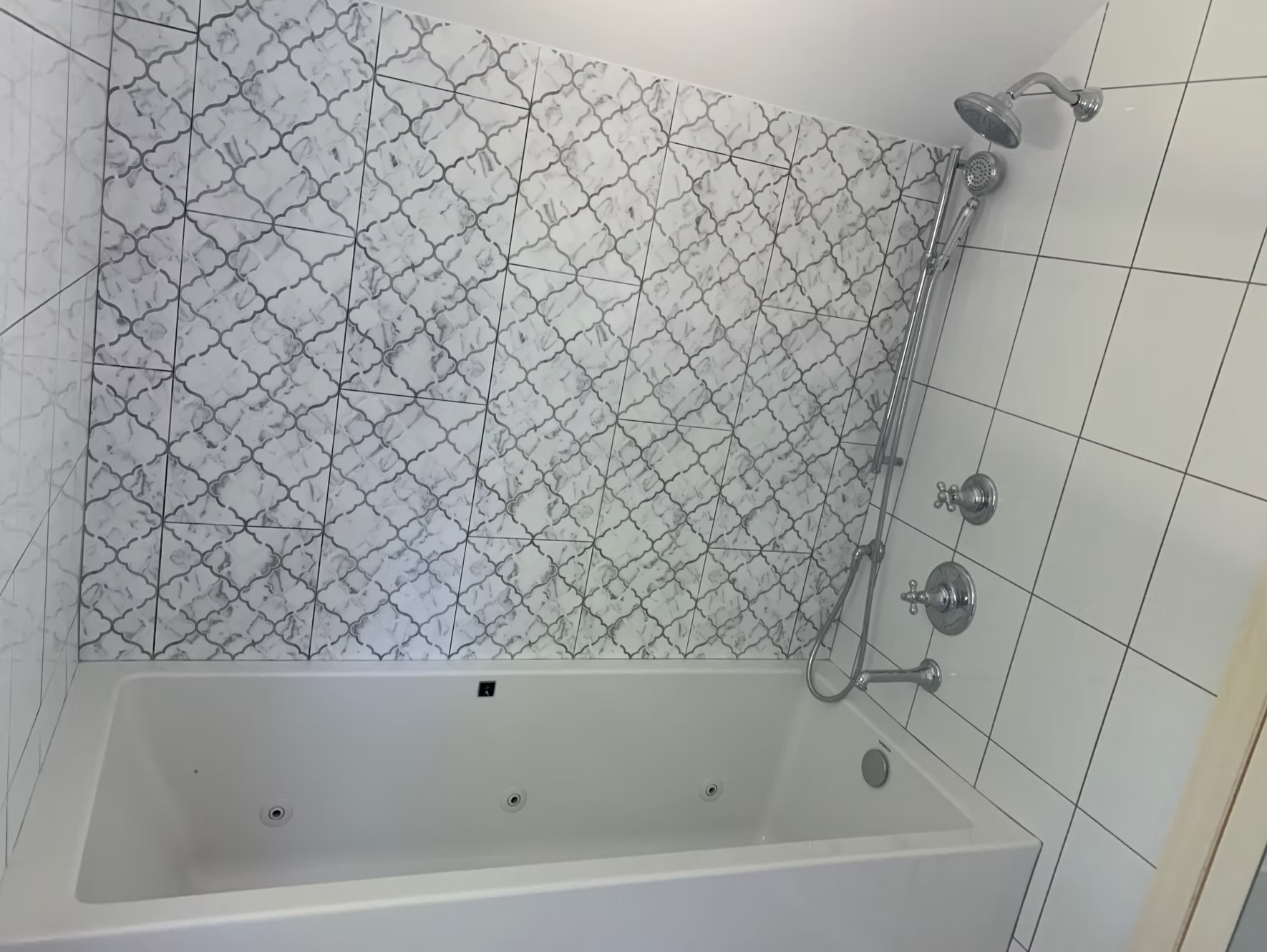 White tiled bathroom with jacuzzi tub and patterned wall tile. Chrome shower fixtures.