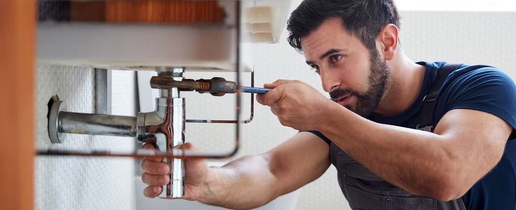 Man fixing plumbing under a sink with a wrench.