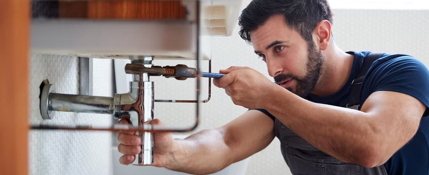 Man fixing plumbing under a sink with a wrench.