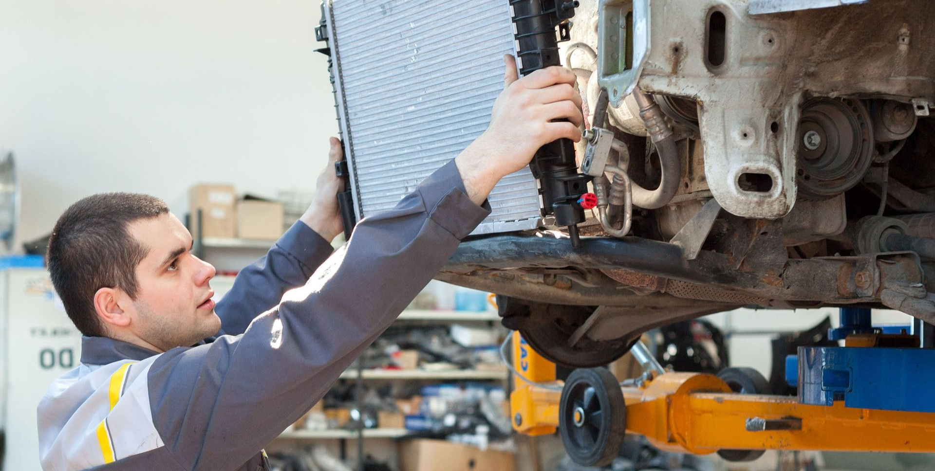 A technician in a uniform installs a car radiator into a vehicle chassis in a repair shop.