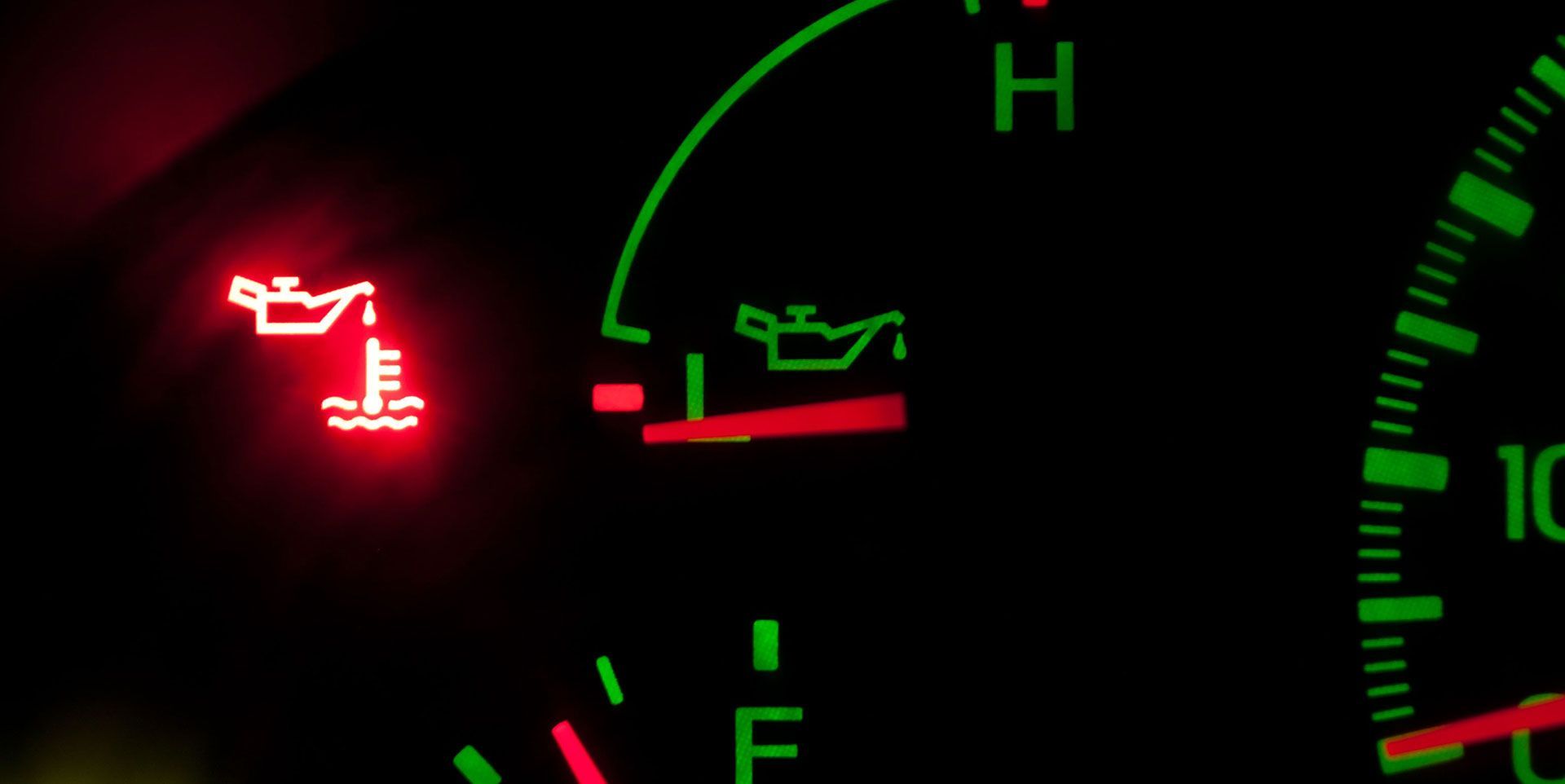A car dashboard warning light shows a red oil can symbol above a thermometer, indicating low oil pressure or high heat.