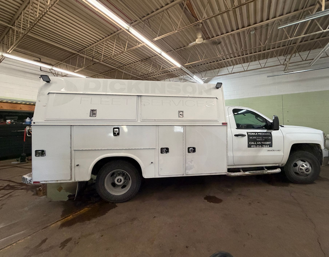 A white utility truck with a service body parked inside a brightly lit warehouse.