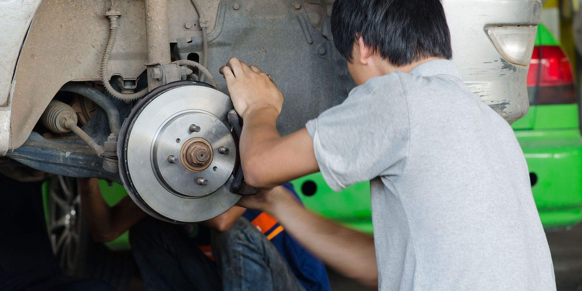 A mechanic in a grey shirt repairs the disc brake assembly of a car in a workshop.