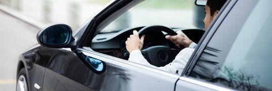 Man driving a black car, hands on the steering wheel.