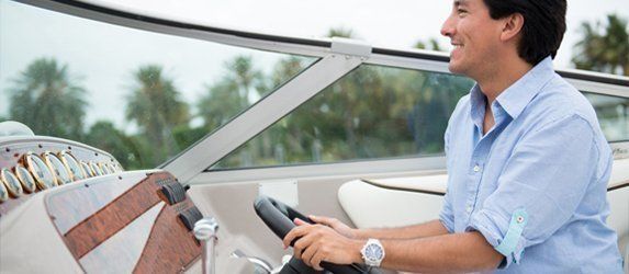 Man smiling while steering a boat with palm trees in the background.