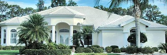 White stucco house with a white tiled roof and tropical landscaping.