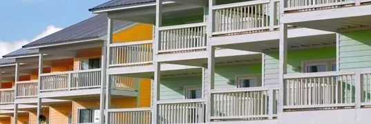 Row of colorful buildings with balconies, painted in orange, yellow, and green, against a blue sky.