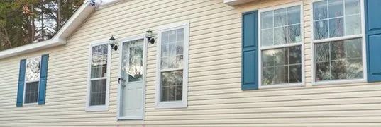 Cream-colored house with blue shutters and a white door. The setting is outdoors.