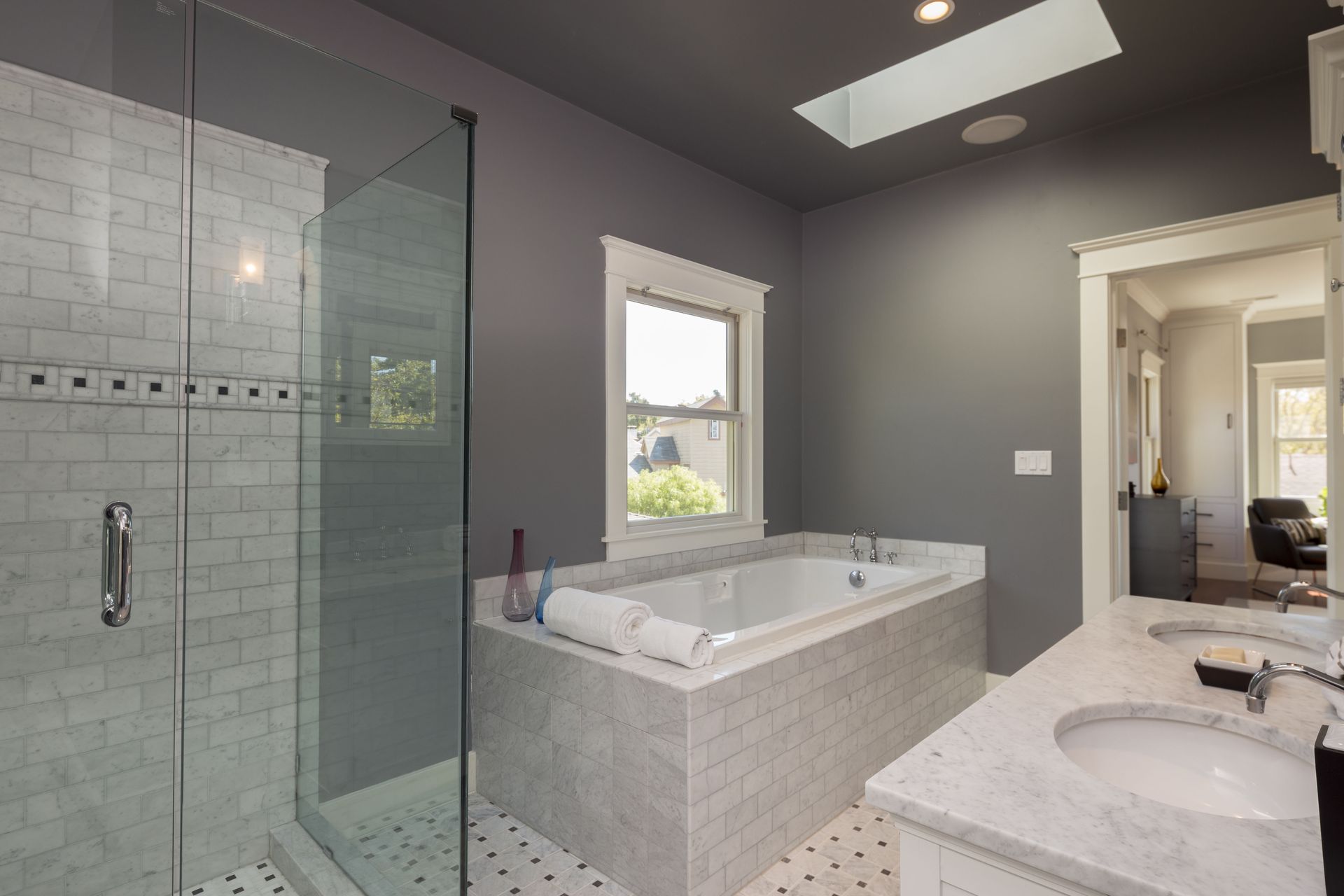Bathroom with a white bathtub, showerhead, and tiled walls.  Built-in shelves are on the left, and recessed ceiling lights illuminate the space.