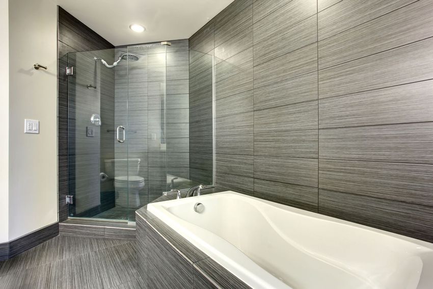 A white bathtub built into a beige tiled wall. The shower head hangs above.