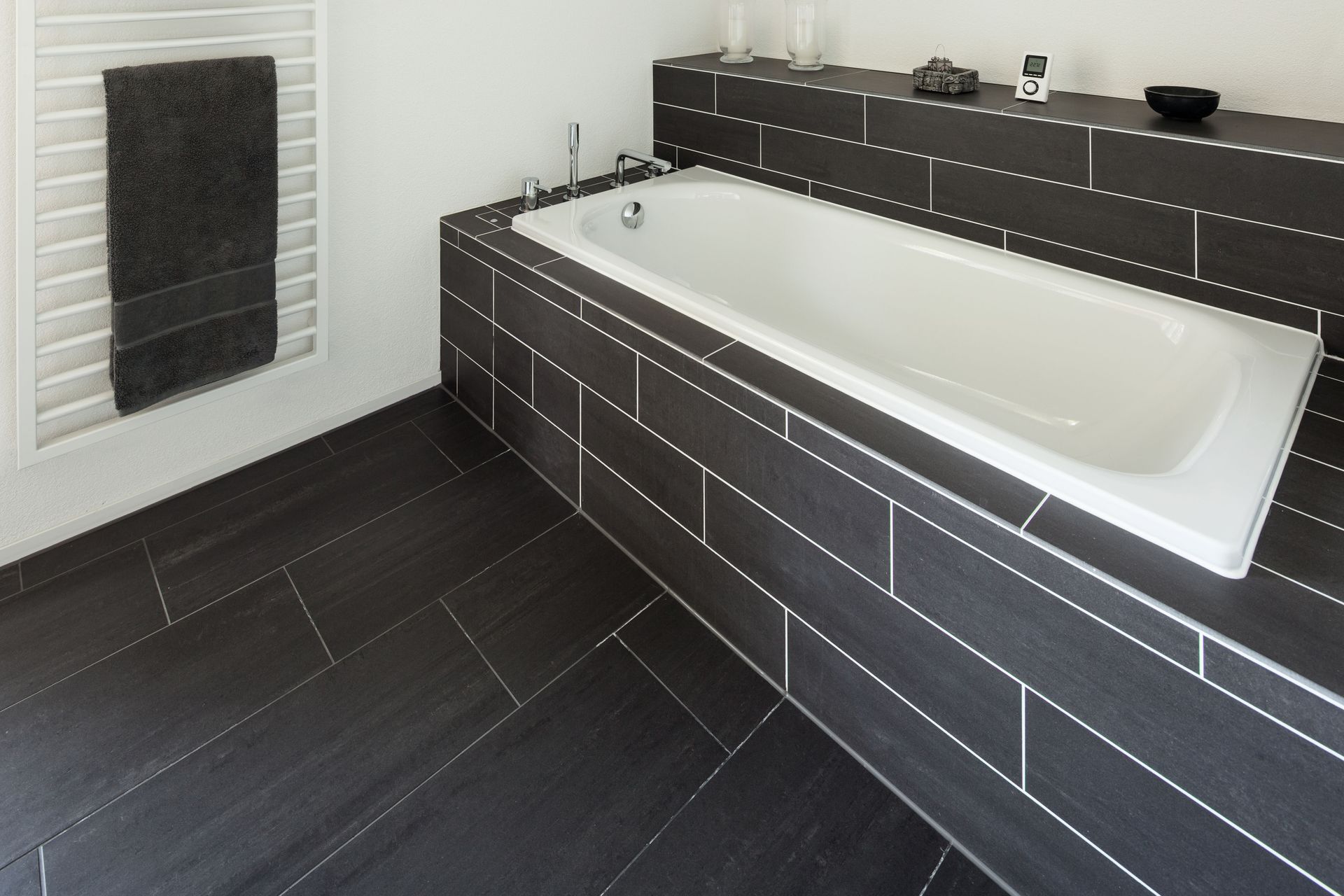 Bathroom with a white bathtub, showerhead, and tiled walls.  Built-in shelves are on the left, and recessed ceiling lights illuminate the space.