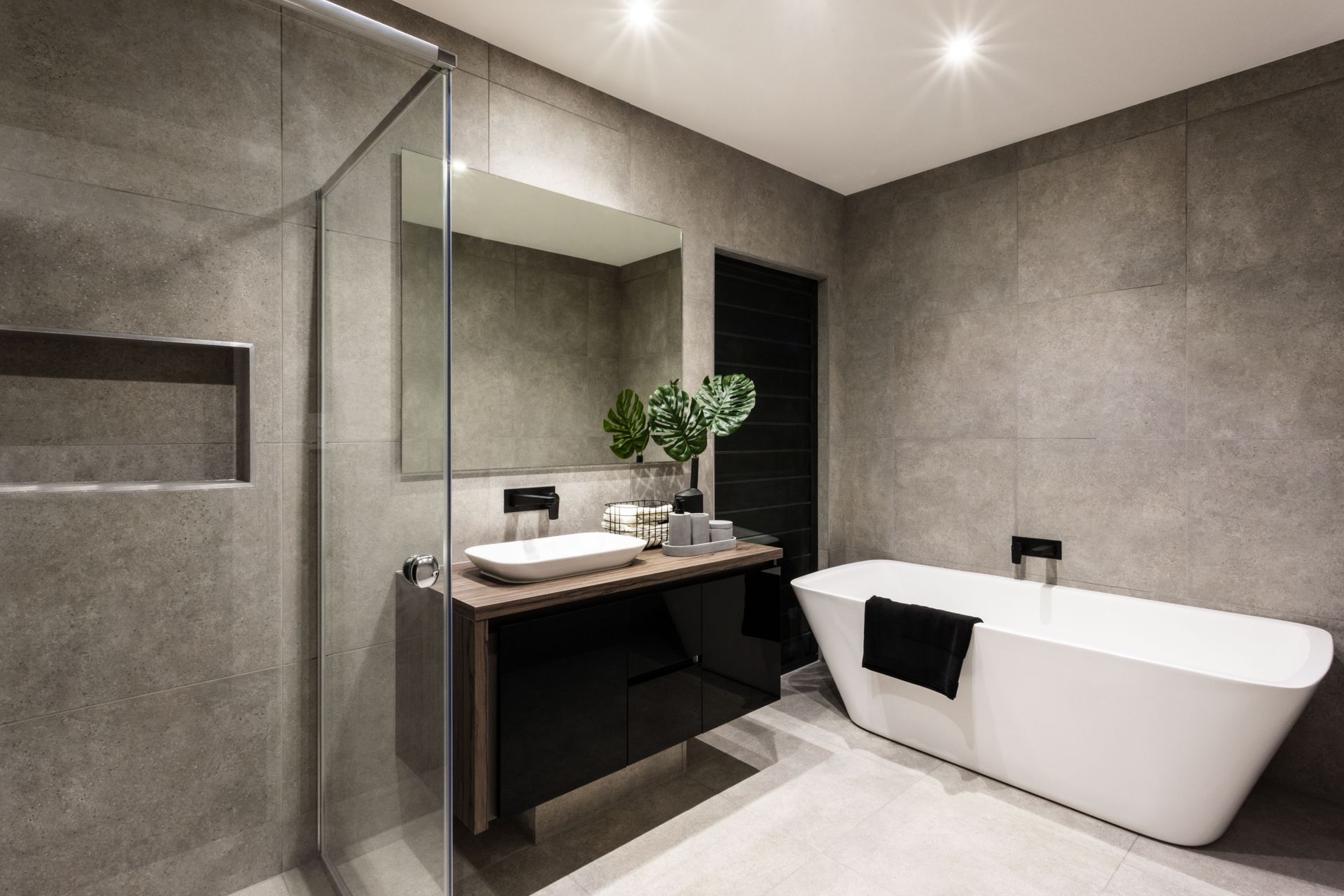 Bathroom with a white bathtub, showerhead, and tiled walls.  Built-in shelves are on the left, and recessed ceiling lights illuminate the space.