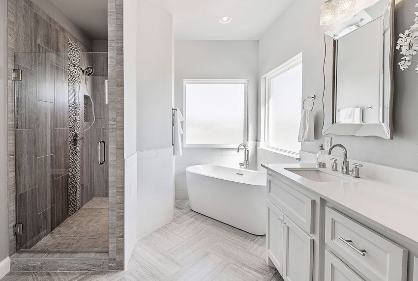 A white bathtub built into a beige tiled wall. The shower head hangs above.
