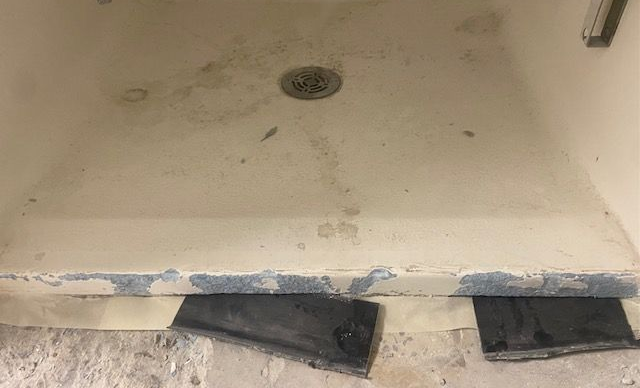 White shower wall with a vertical crack, near wooden framing - before