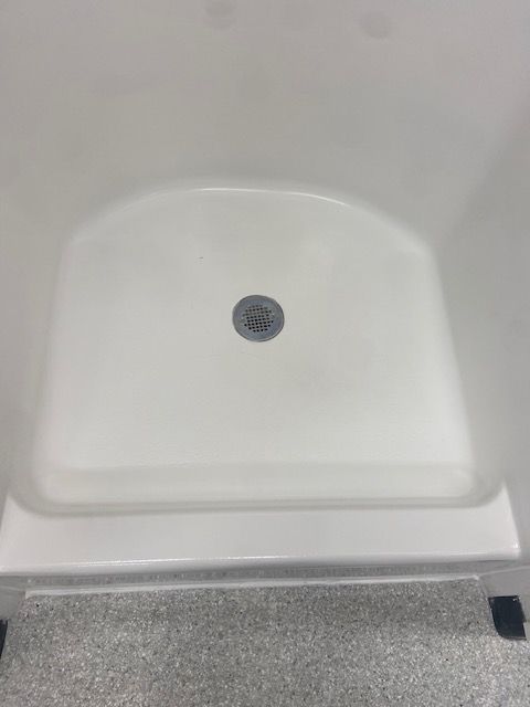 A white, low-profile walk-in shower stall floor with a central drain.