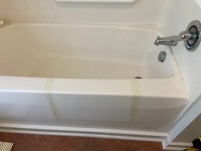 White bathtub with a faucet and drain. Some masking tape is visible on the tub's front.