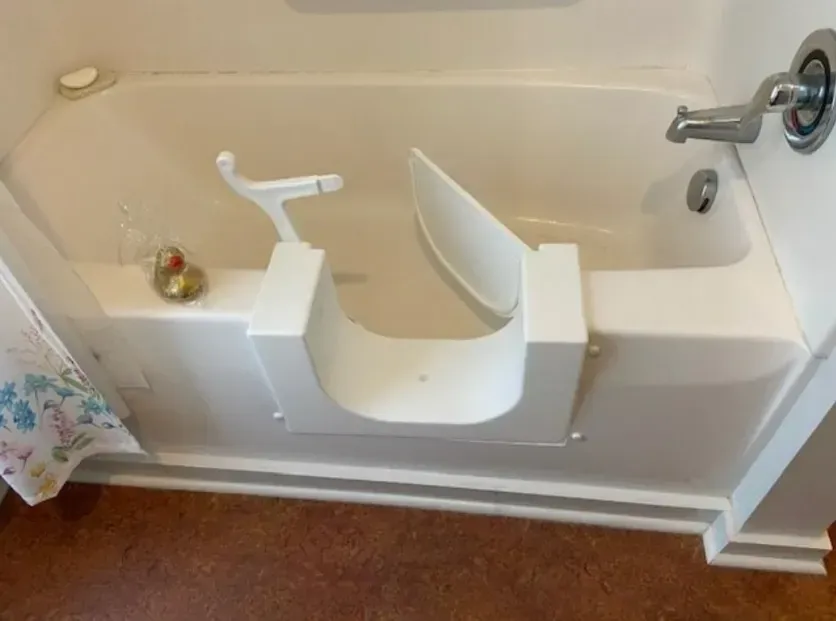 White walk-in bathtub with a hinged door and seat. Faucet and showerhead on the right.