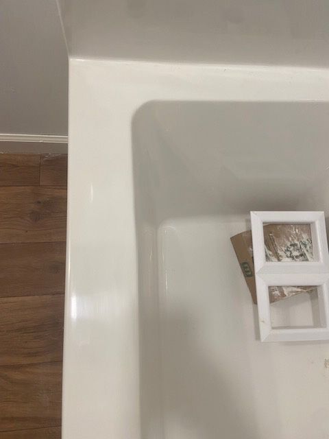 White bathtub with a frame sitting inside, next to a wooden floor.