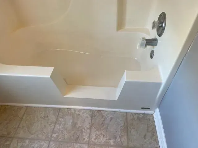 Beige alcove bathtub with a step-in feature, next to a light blue wall and brown tiled floor.