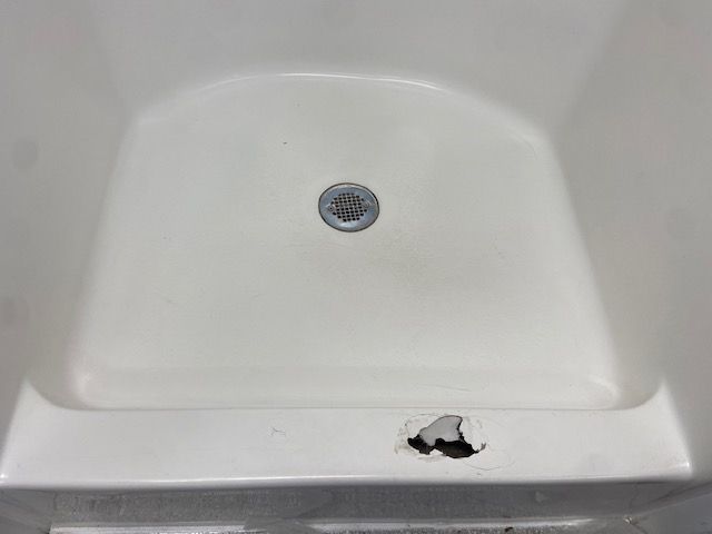 A white shower base with a large, jagged hole in the front threshold.