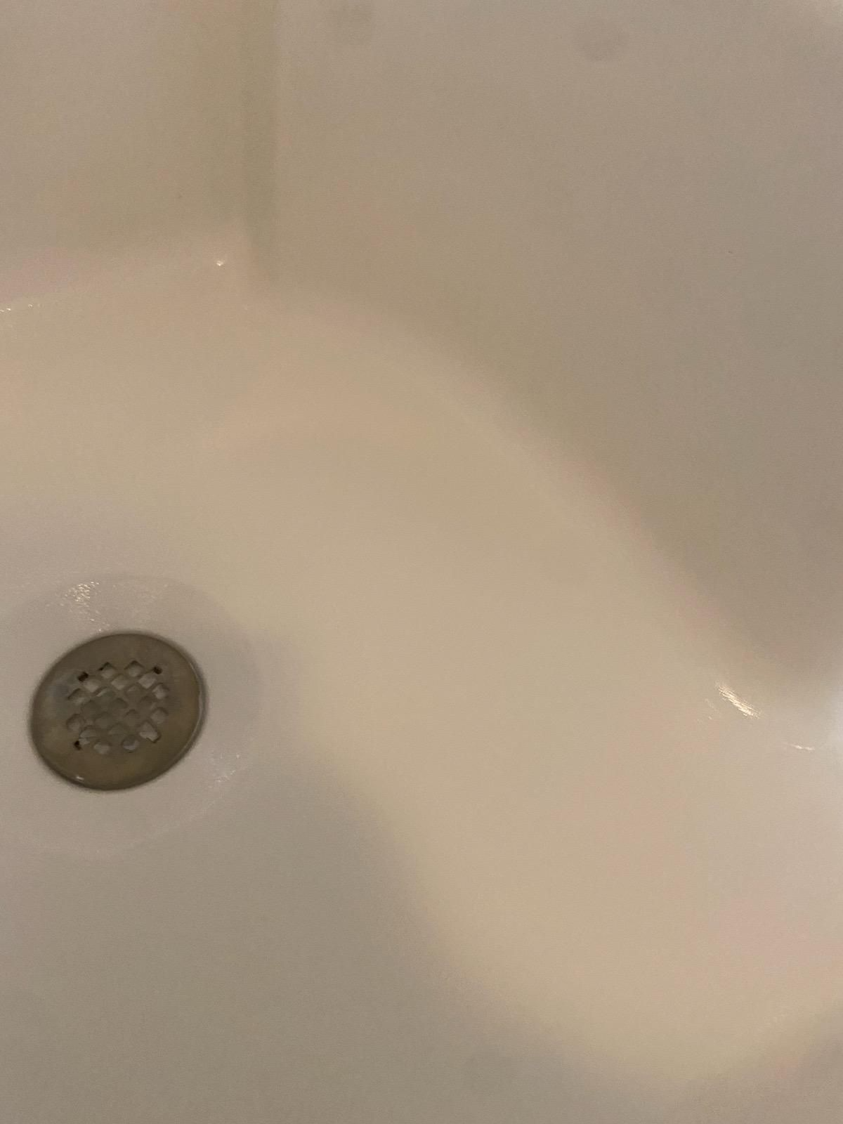 Close-up of a white sink with a drain in the lower left corner.