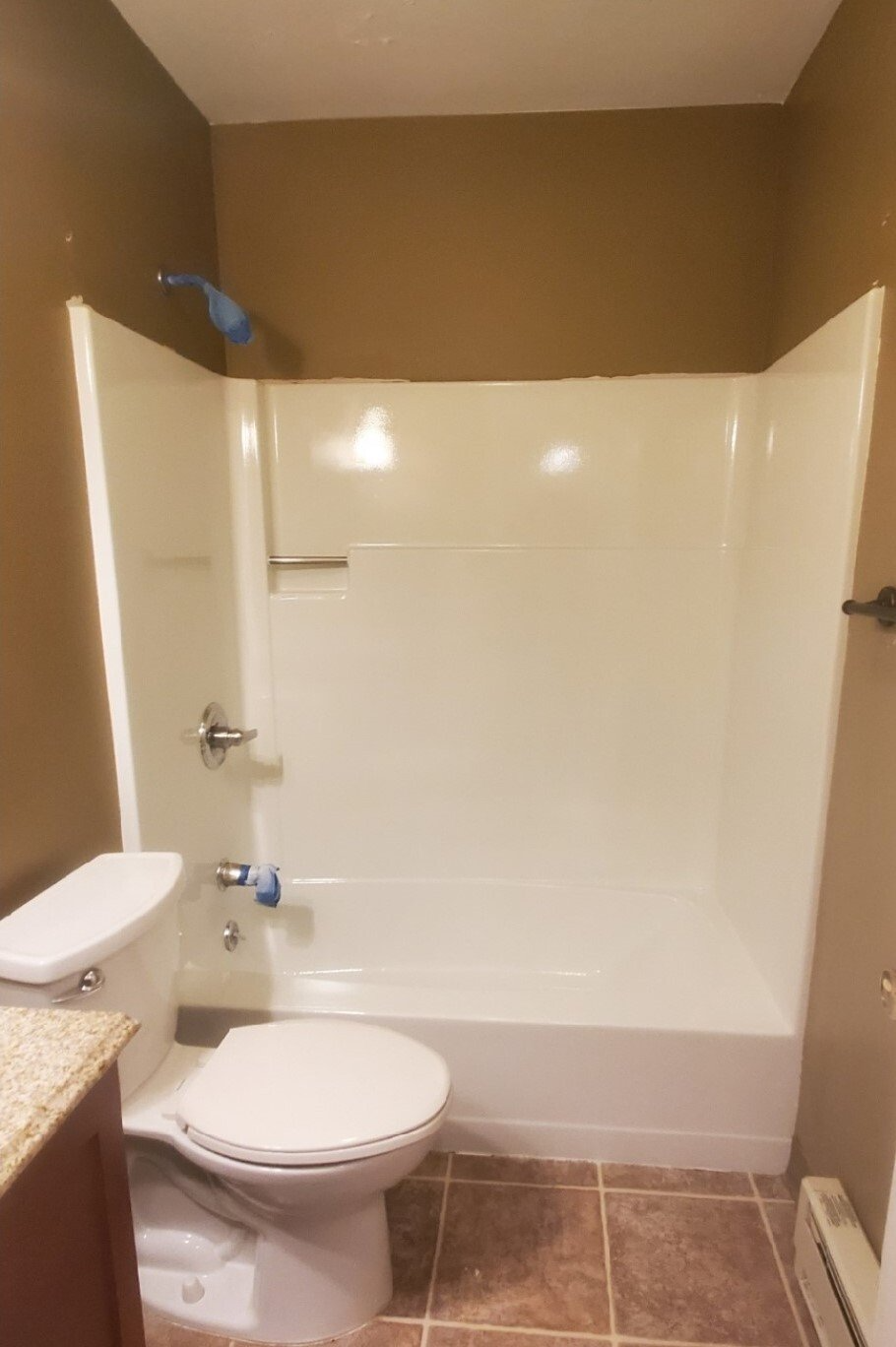 Bathroom with a white tub and toilet, brown walls, and tile floor. The showerhead is blue.