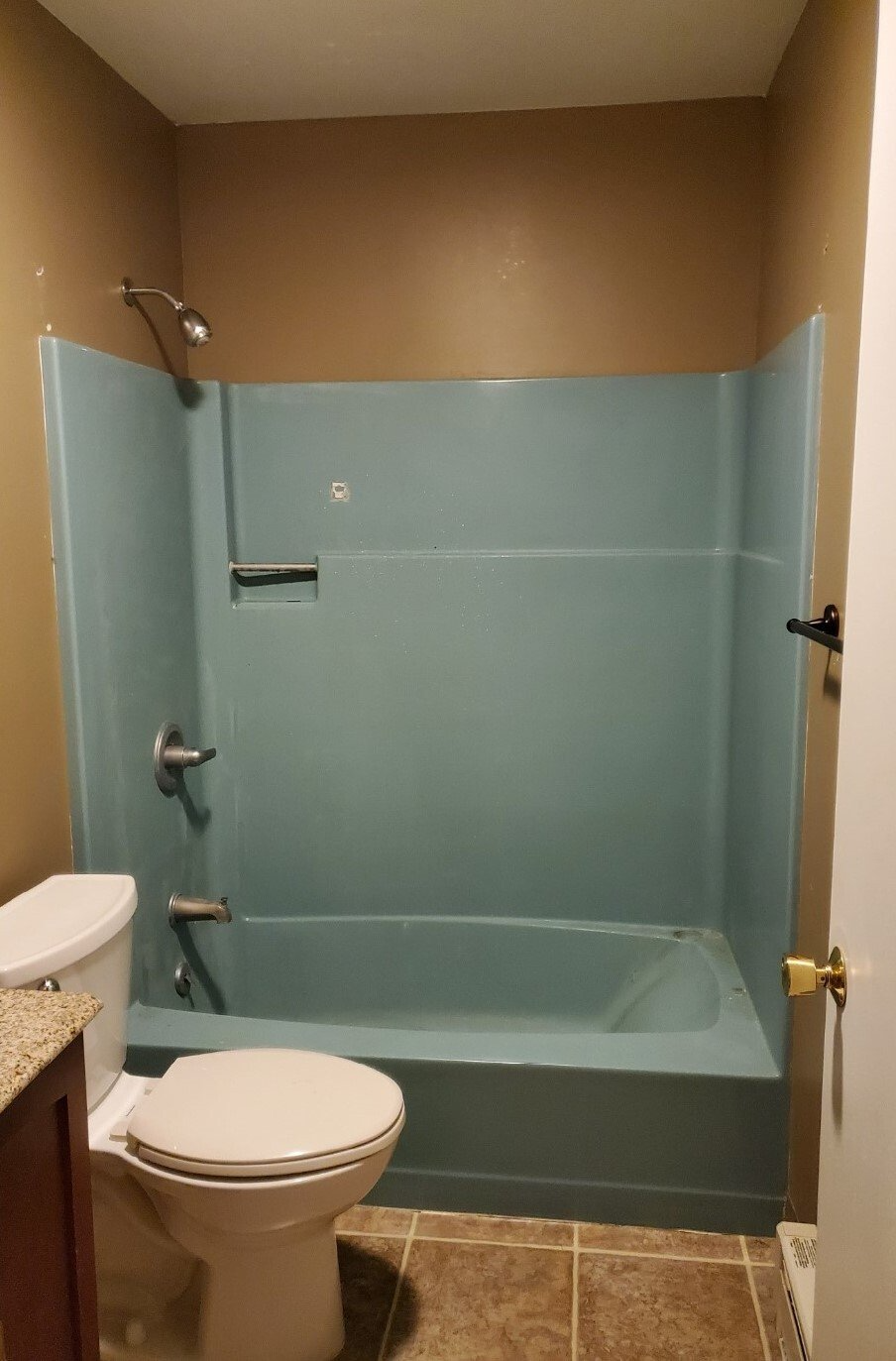A small bathroom with a blue tub and shower surround. A toilet sits to the left, and the walls are tan.