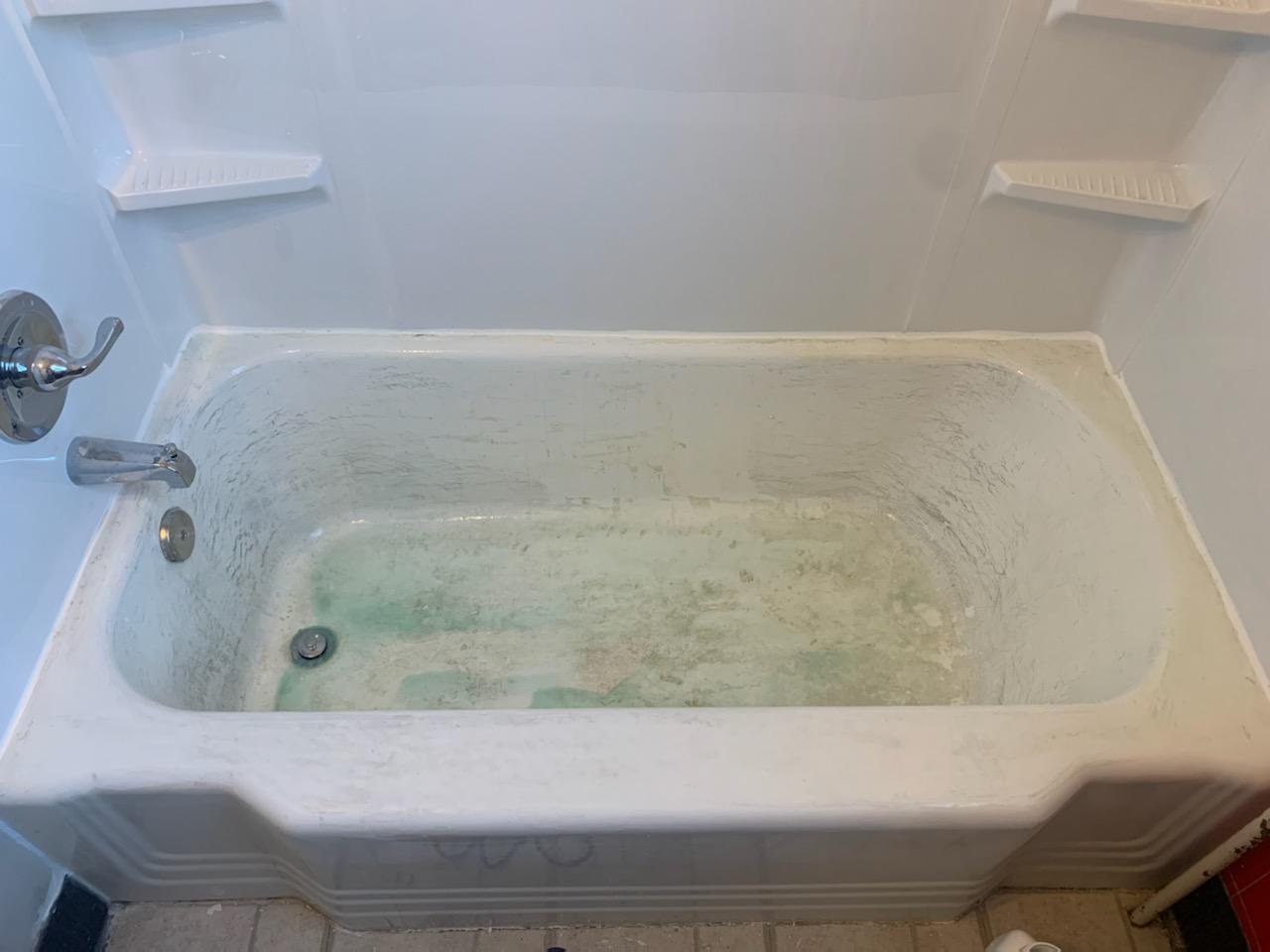 Dirty white bathtub with green mildew stains in a bathroom, seen from an elevated angle. Faucet and two built-in shelves are visible.