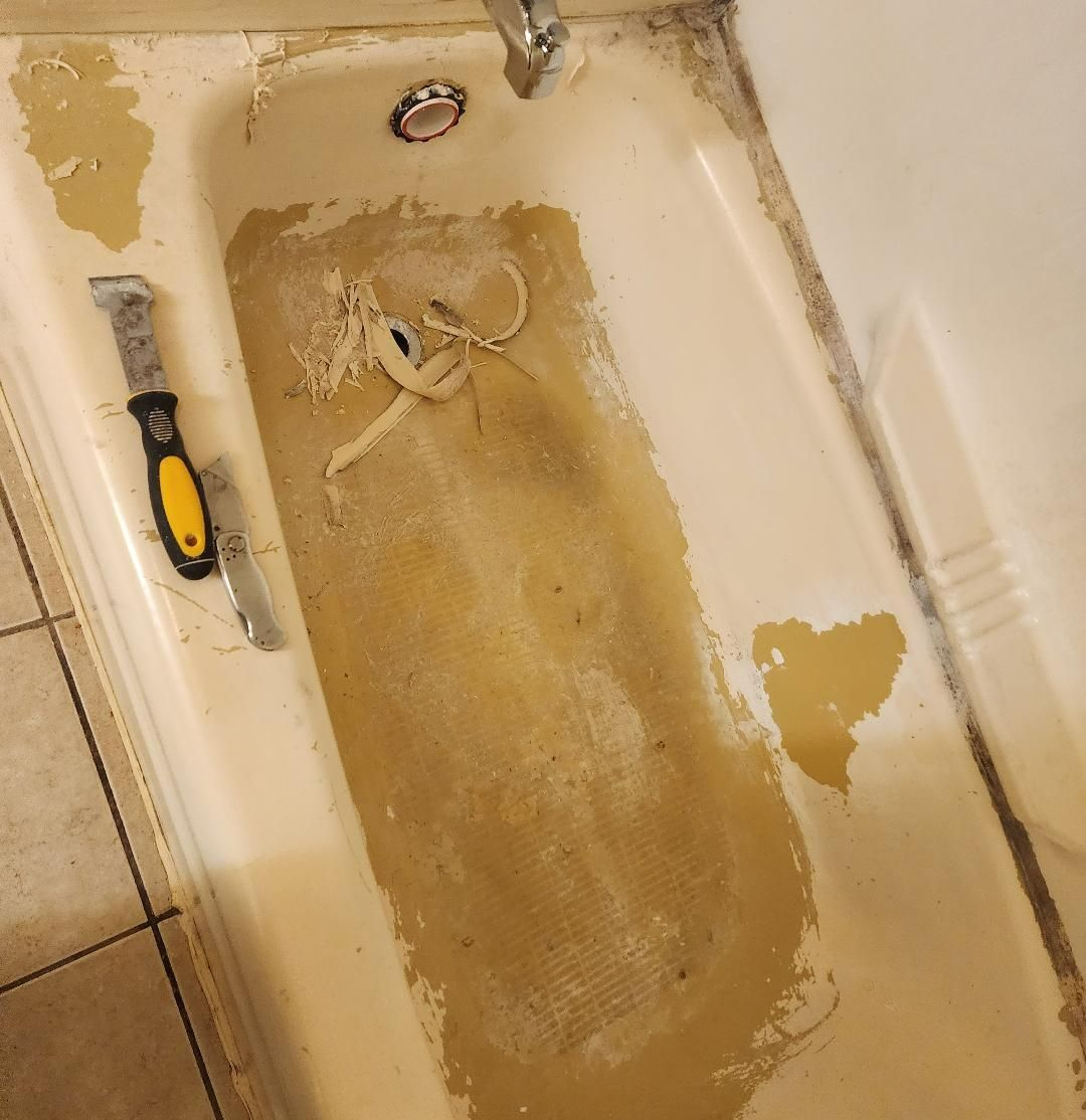 A bathtub with peeling paint and a scraper tool inside. The tub is dirty and stained with a visible drain.