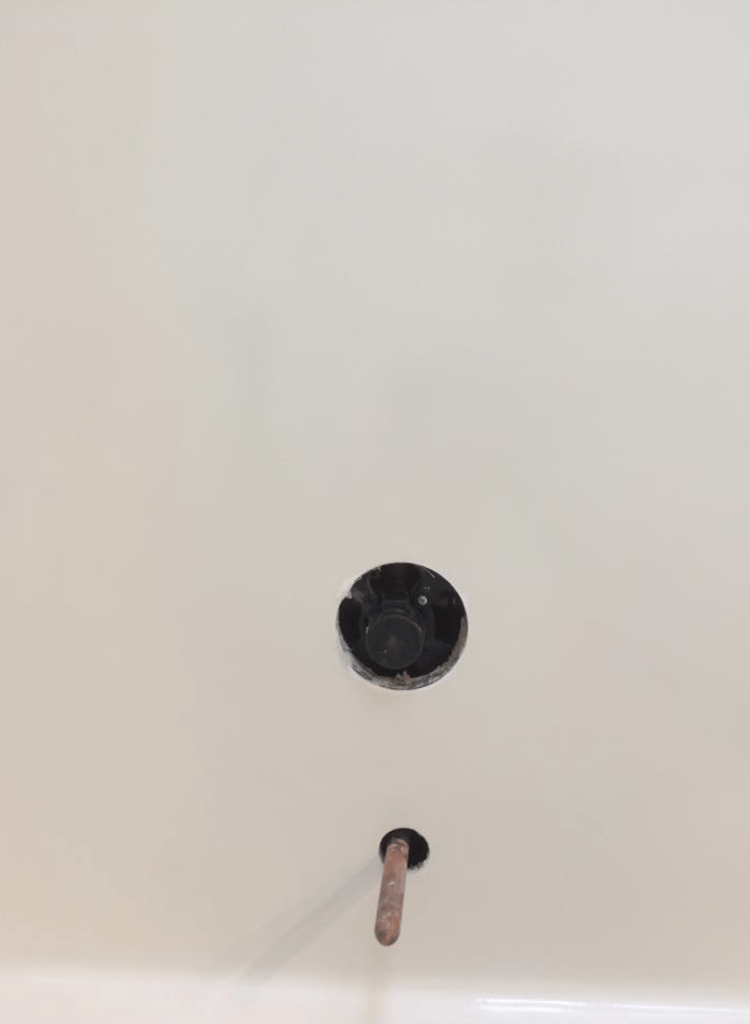 A close-up of a bathtub's drain and overflow with a visible pipe. The drain is dark and the tub is white.