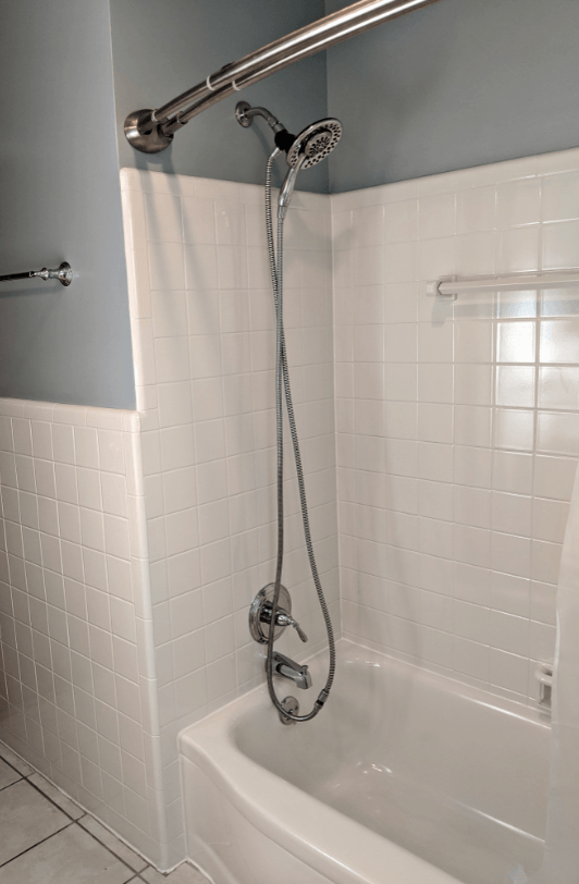 White tiled shower/tub with silver fixtures, including a handheld showerhead and a rain showerhead mounted on a blue wall.