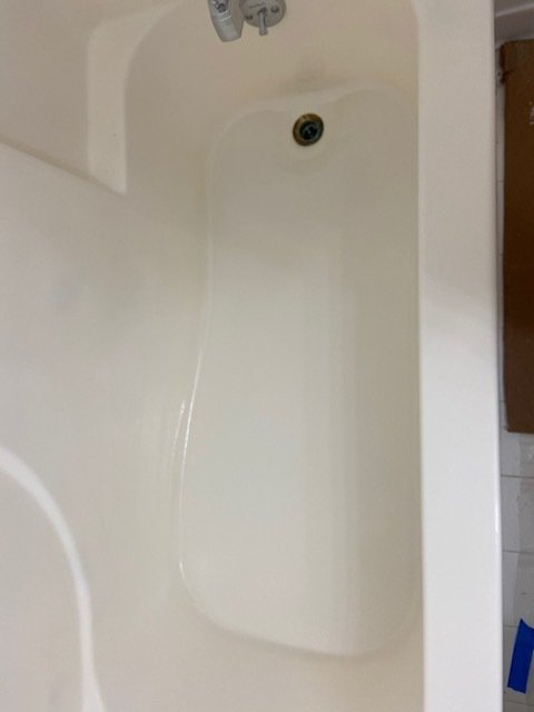 A white bathtub with a drain in the center. The showerhead is visible above.