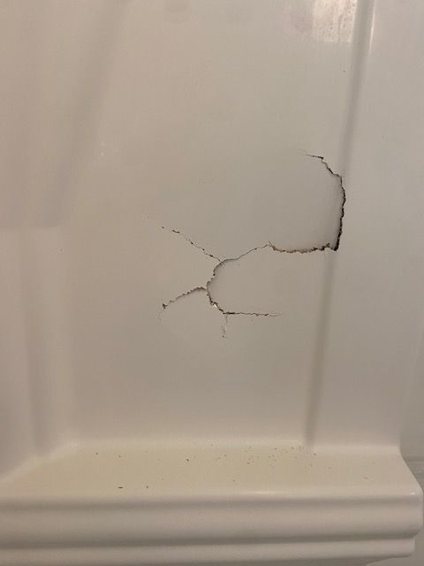 Close-up of a white wall with a large crack and visible damage near the center.