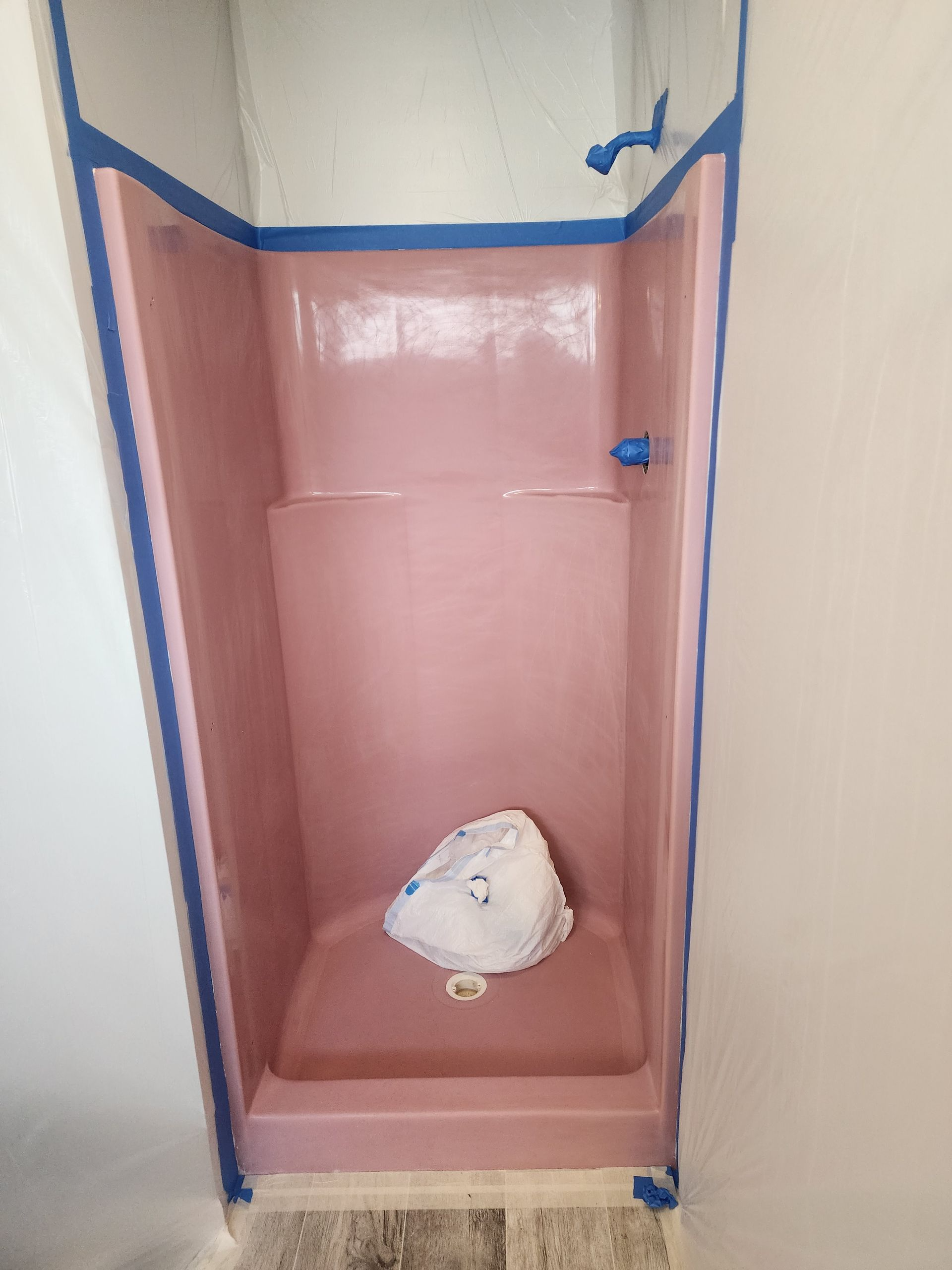 Pink shower stall with blue painter's tape applied, a white bag sits inside.